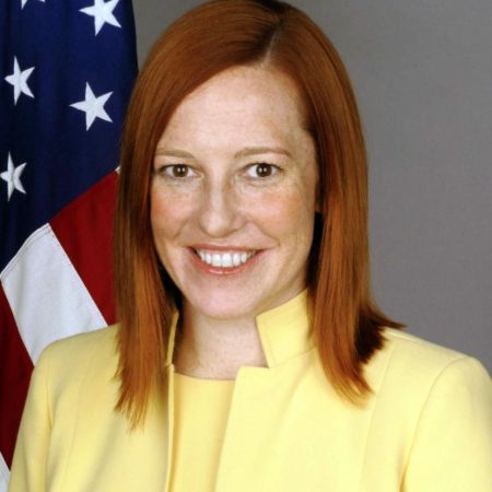 Jen Psaki in a yellow coat poses for a picture.